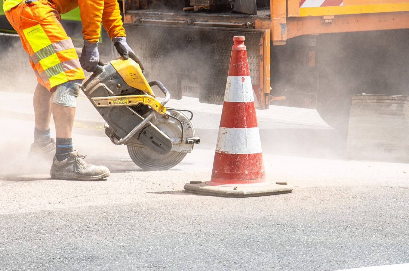 Road construction worker cutting asphalt with safety cones nearby